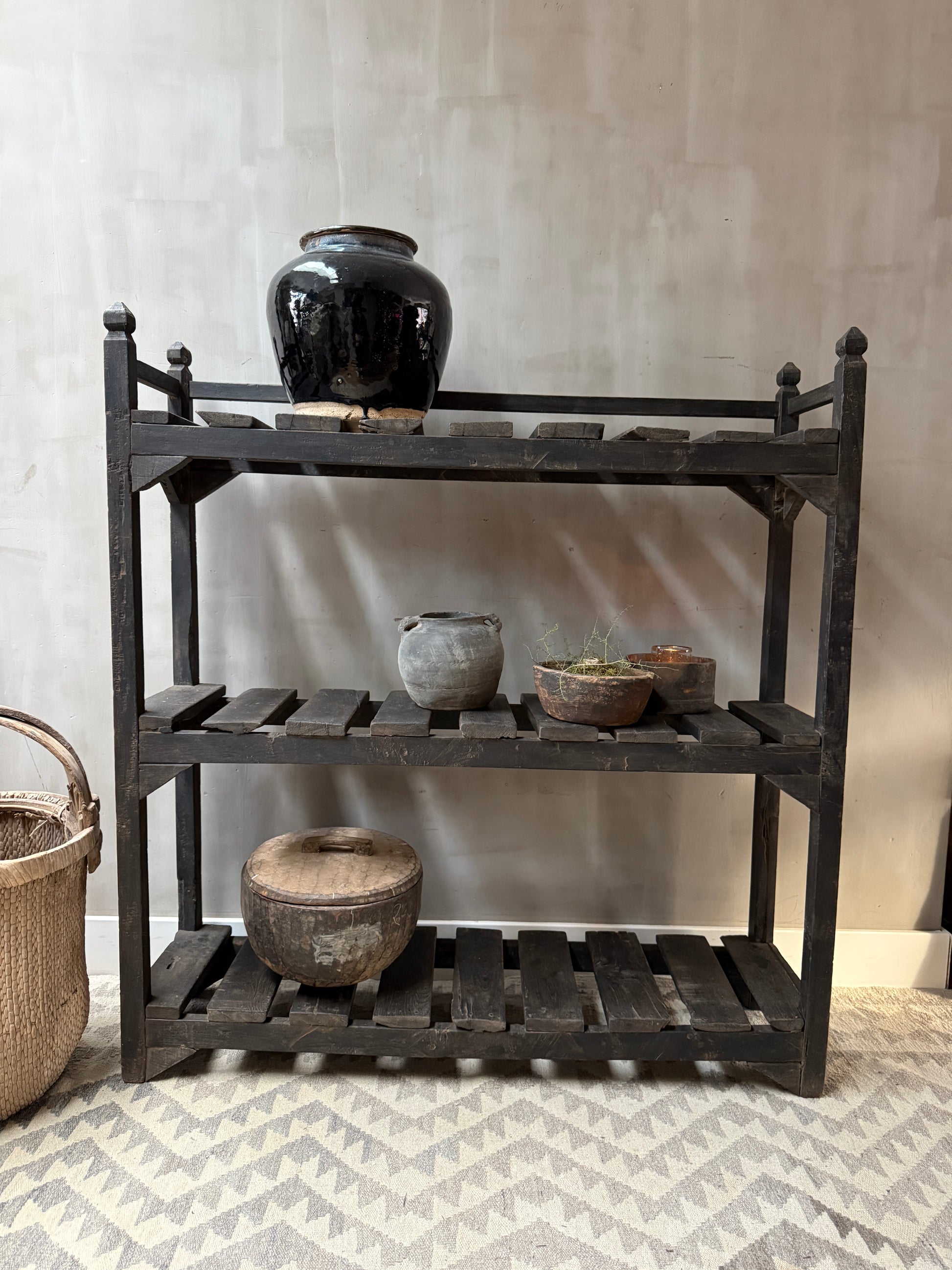 Zwarte houten plankenkast met handgemaakte potten en mand, landelijk sober interieur