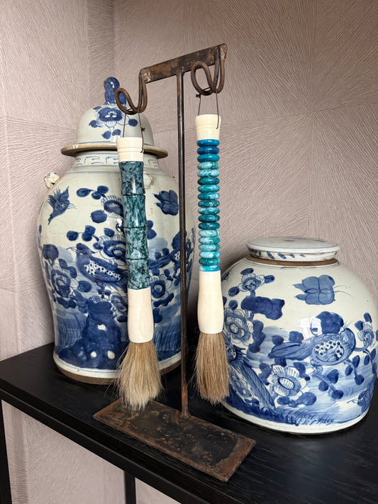 Handgemaakte landelijke woonaccessoires: blauwe kwasten en porseleinen potten op zwarte plank