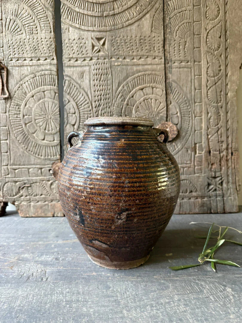 Authentieke bruine, handgemaakte aardewerken pot voor sober landelijk interieur op houten ondergrond.