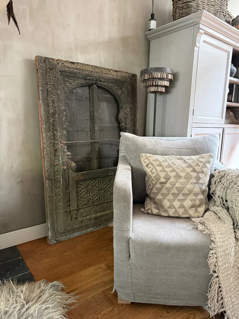 Landelijke woonkamer met grijs linnen fauteuil, handgemaakt houten paneel en sobere woonaccessoires