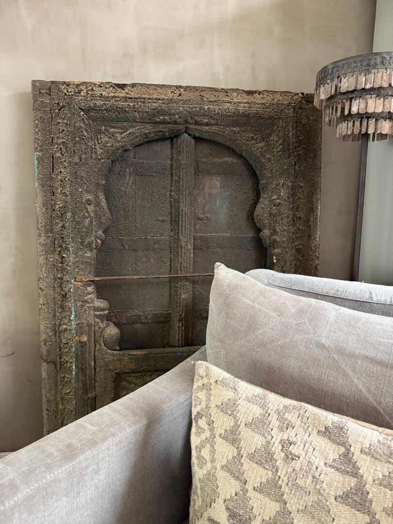 Authentieke houten deur uit India achter beige bank met sierkussen, sober interieurstijl