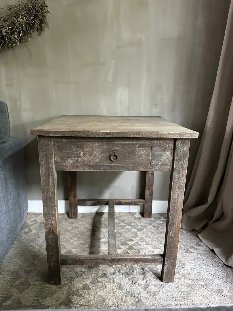 Authentieke, handgemaakte houten tafel met lade in landelijk sober interieur op vloerkleed