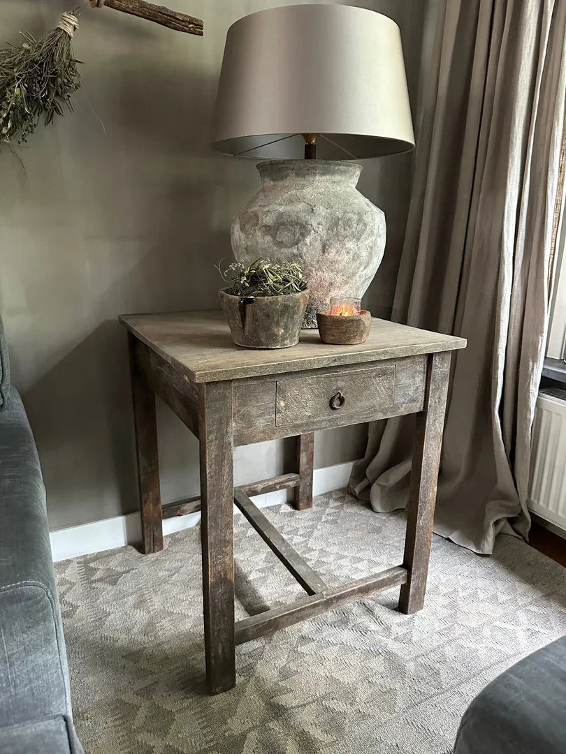 Sober landelijke houten bijzettafel met robuuste lamp en handgemaakte woonaccessoires in woonkamer