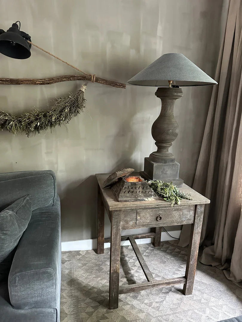 Landelijk sober interieur met handgemaakte houten tafel, grijze bank en decoratieve lamp