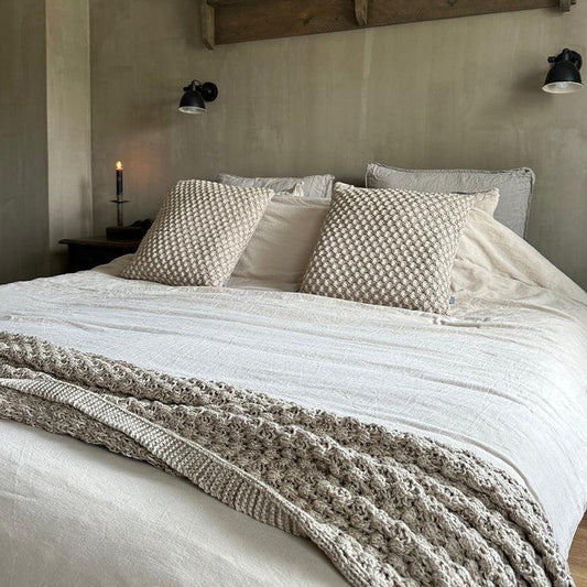 Sober landelijk slaapkamerinterieur met handgemaakte accessoires en gebreide kussens.