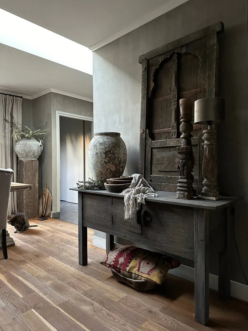 Landelijke, sobere woonkamer met handgemaakte houten tafel, oude kruik, vaas en vintage accessoires