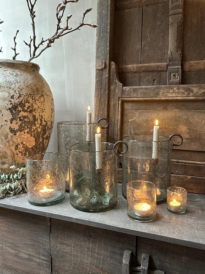 Sober landelijk interieur met handgemaakte glazen windlichten en rustieke kaarsen op houten kast