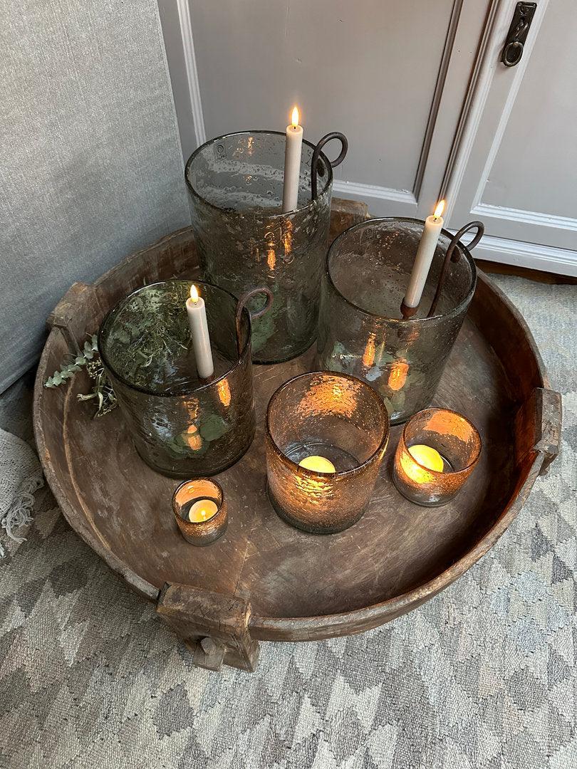 Landelijke handgemaakte glazen windlichten met kaarsen op robuuste houten schaal, sfeervol interieur