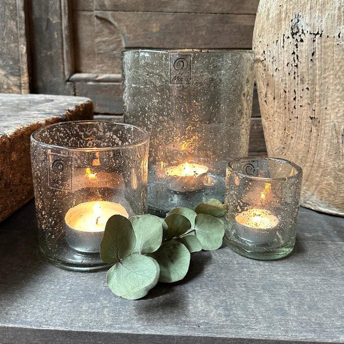 Handgemaakte glazen windlichten met brandende theelichten en eucalyptus, sober landelijk interieur