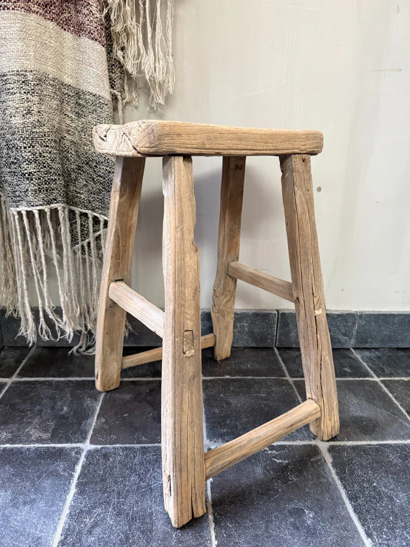 Authentiek handgemaakt houten krukje op donkere tegelvloer, landelijk en sober interieur