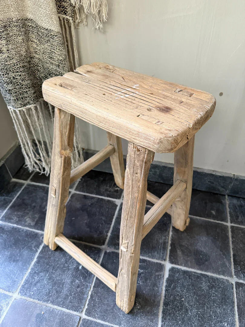 Authentiek handgemaakt houten krukje op donkere tegels, sober landelijk interieur