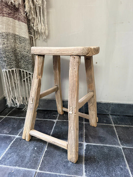 Authentiek, handgemaakt houten krukje op donkere tegelvloer, landelijk sober interieur