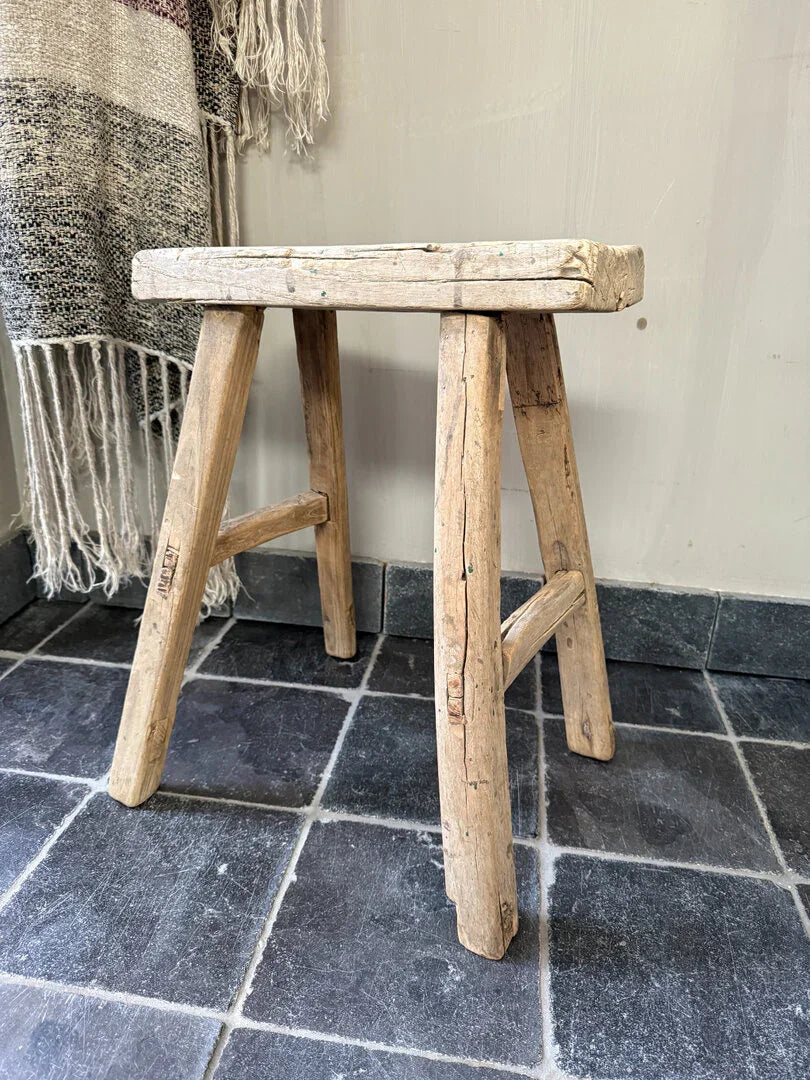 Authentiek handgemaakt houten krukje op donkere tegelvloer, landelijk sober interieur