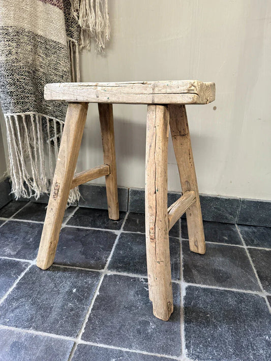 Authentiek handgemaakt houten krukje op donkere tegelvloer, landelijk sober interieur