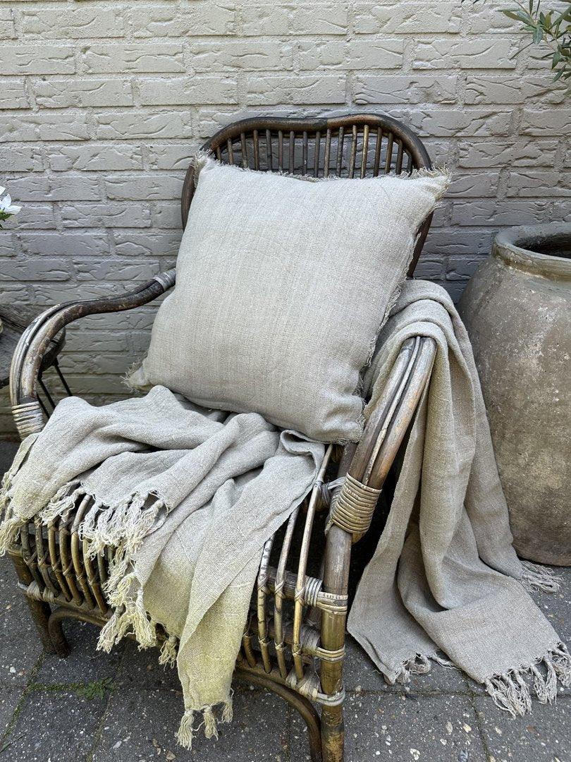 Linnen kussen en plaid in naturel tint op rotan stoel, landelijke en sobere woonstijl