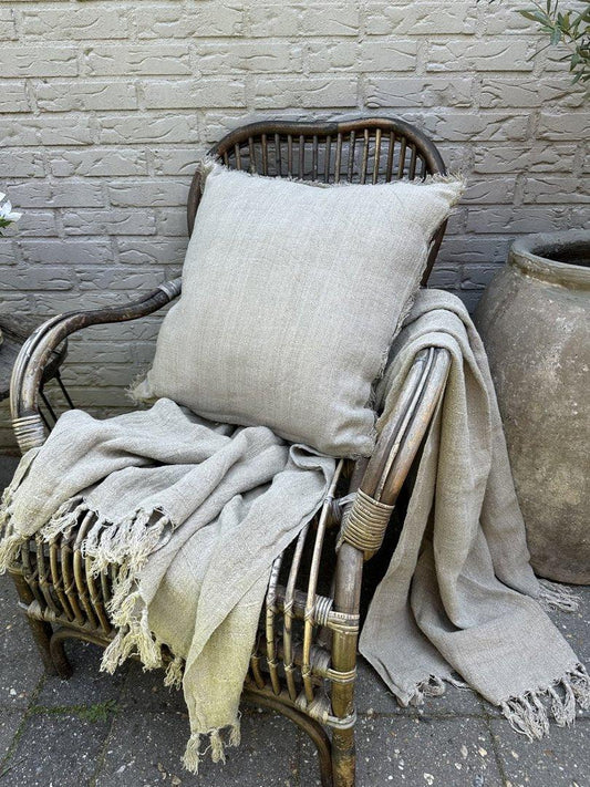 Linnen kussen en plaid in naturel tint op rotan stoel, landelijke en sobere woonstijl