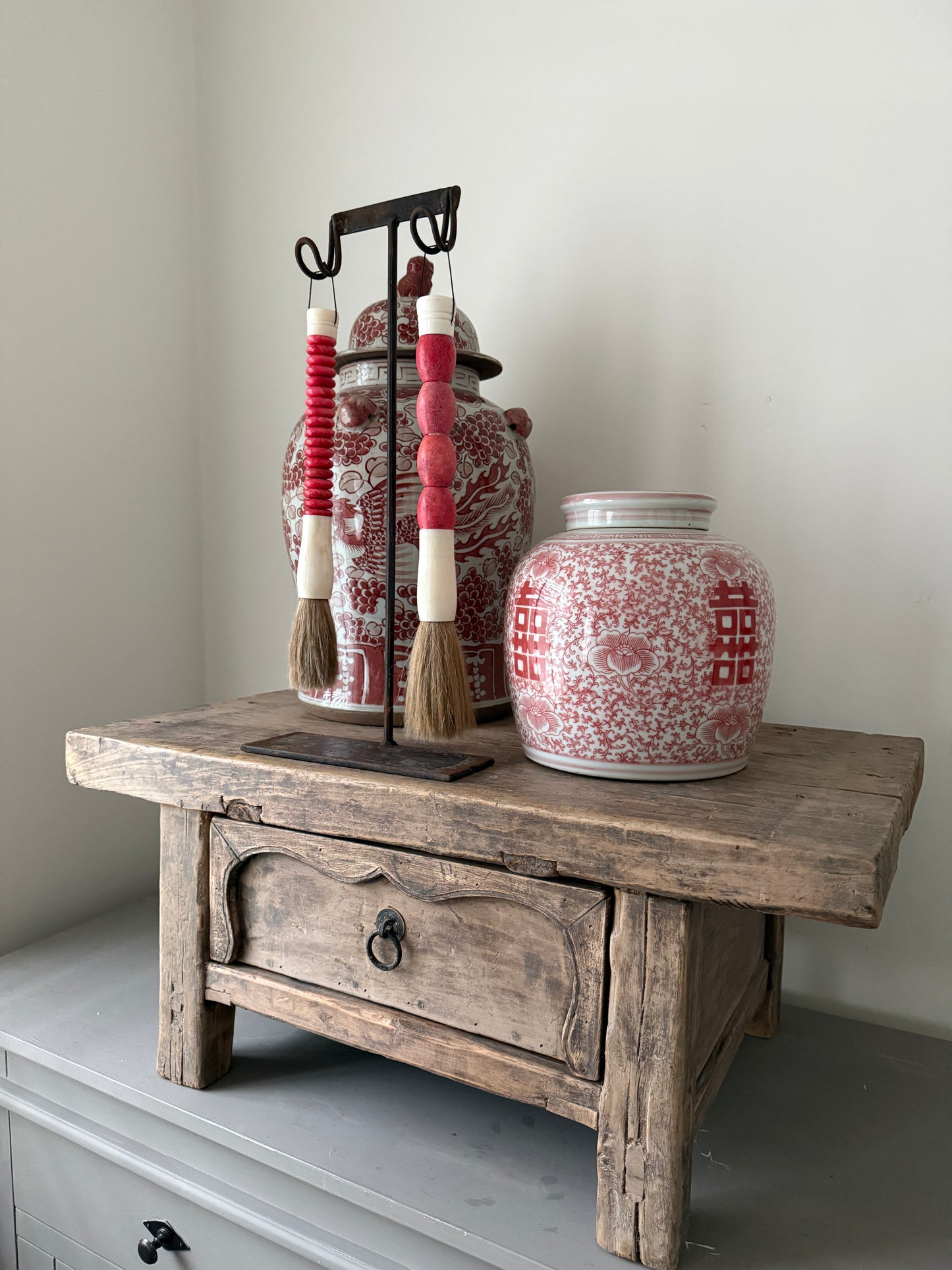 Handgemaakte decoratiekwasten en porseleinen vazen op robuust houten tafeltje, landelijk sober interieur