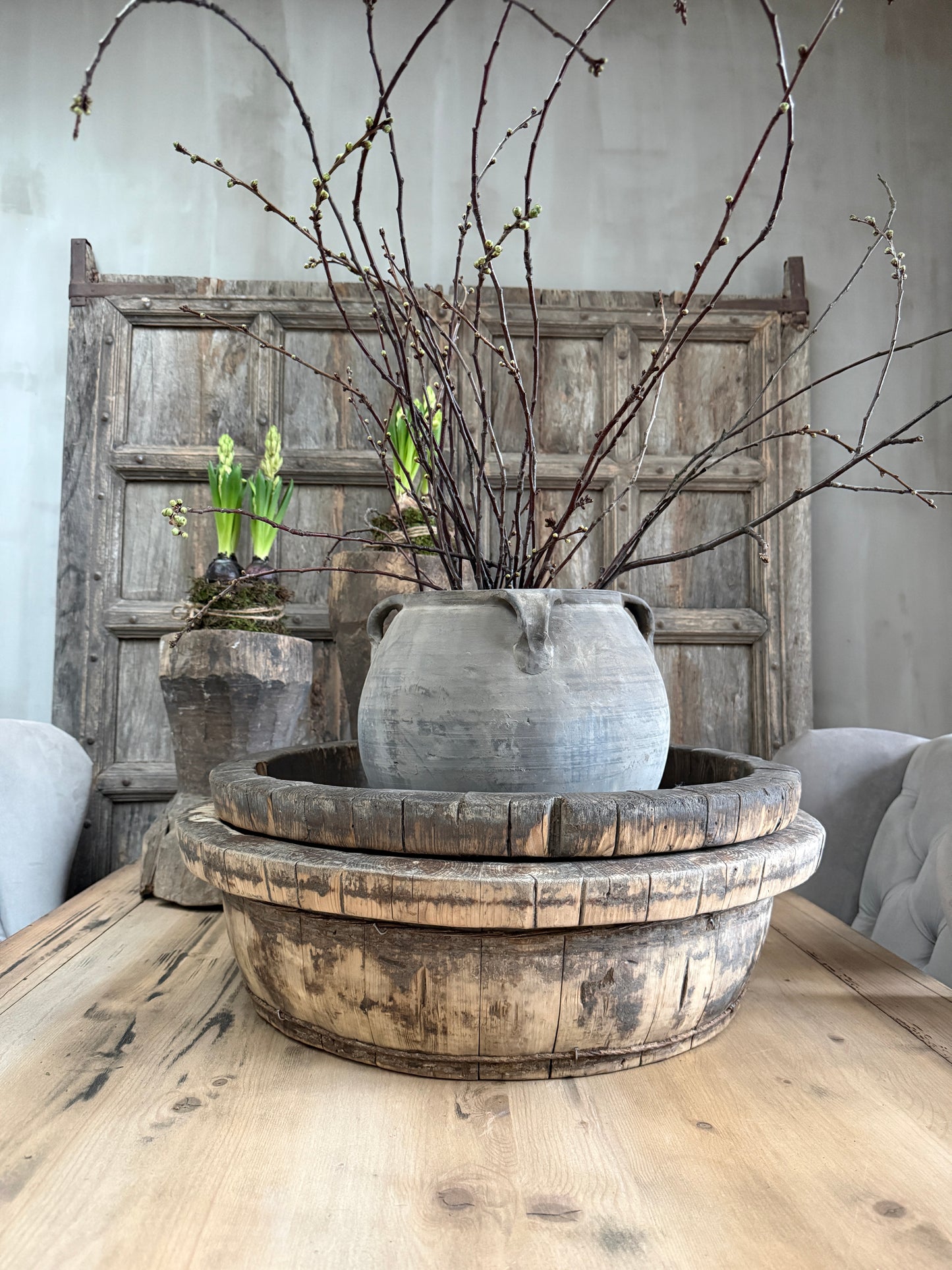 Authentieke olijfbak met kruik en takken op houten tafel, sober landelijk interieur