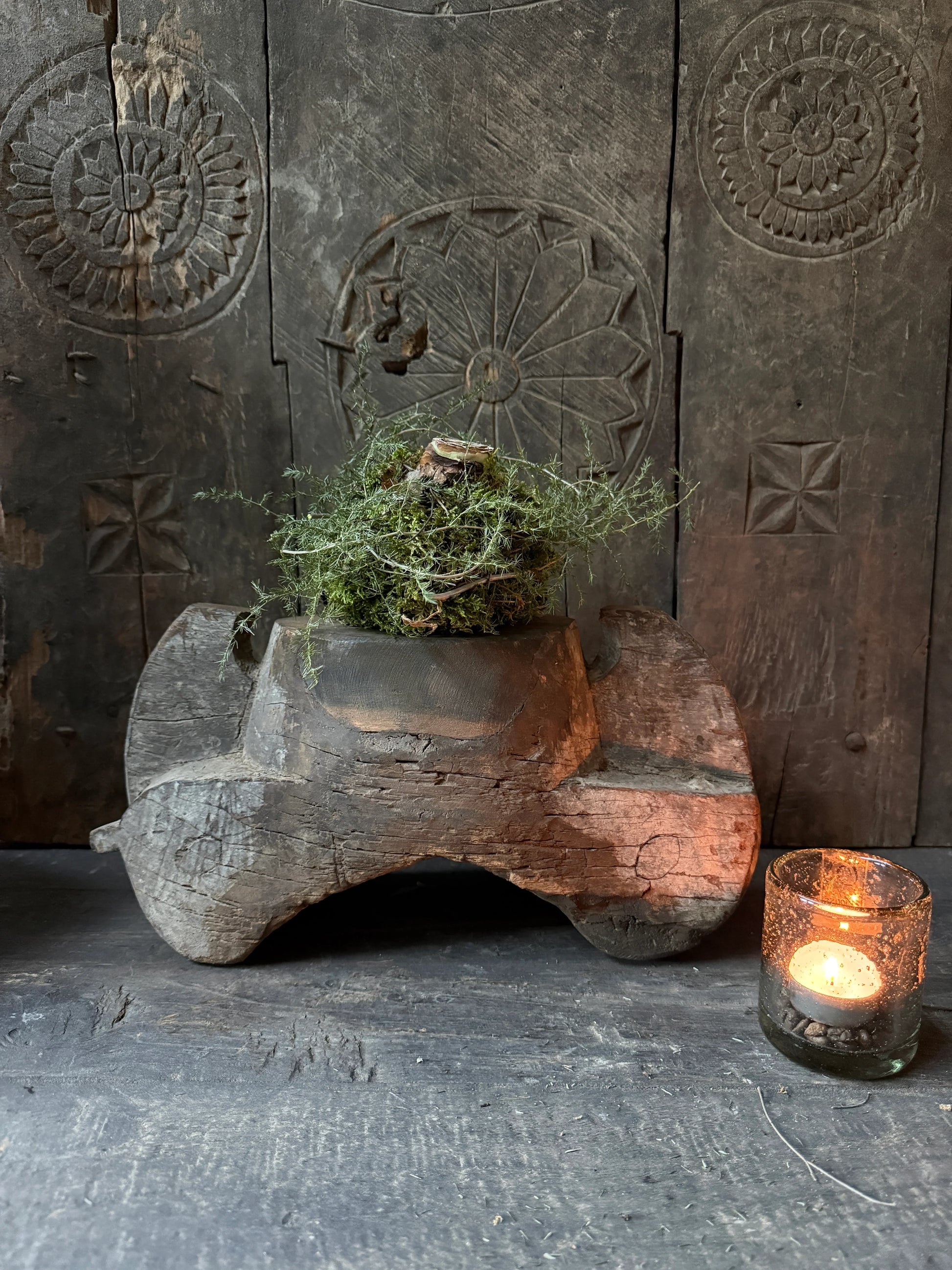 Authentieke houten kandelaar met mosdecoratie en glazen windlicht op sobere houten ondergrond