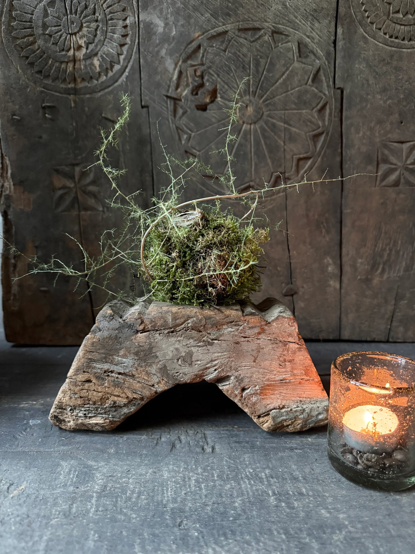 Rustieke houten ornamentkandelaar met plant en brandend theelichtje, sober landelijk interieur