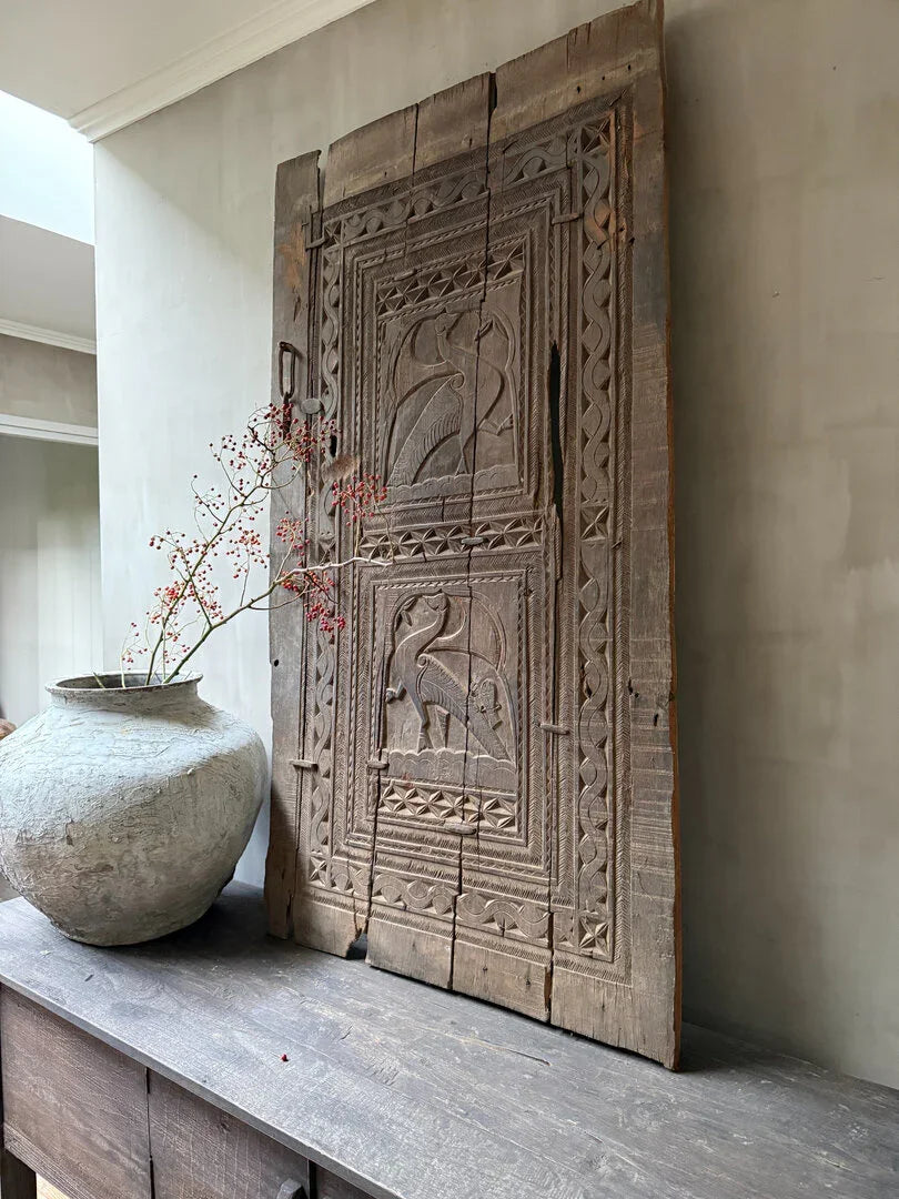 Handgemaakt houten paneel met uitgesneden vogels, landelijke vaas op houten tafel, sober interieur