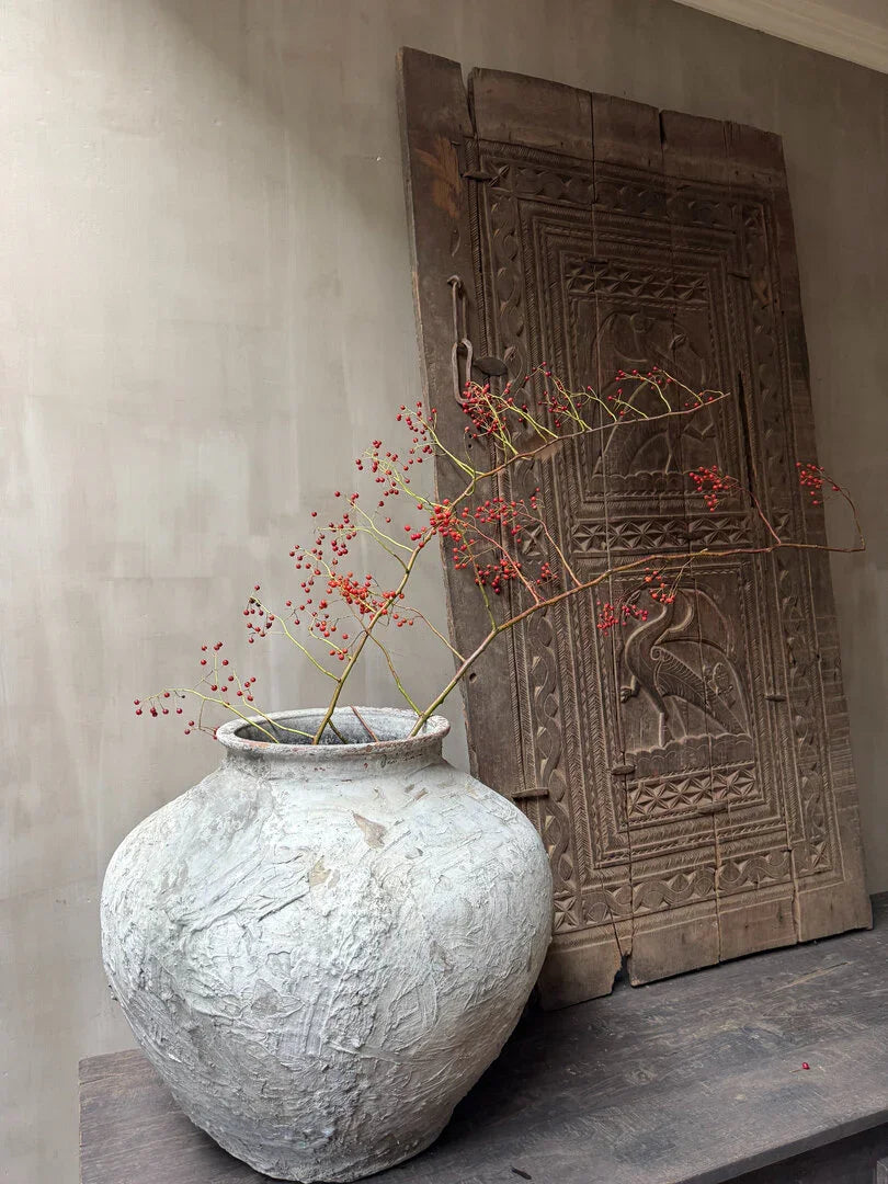 Authentieke, handgemaakte vaas met rode bessen takken en houten paneel, sober landelijke woondecoratie.
