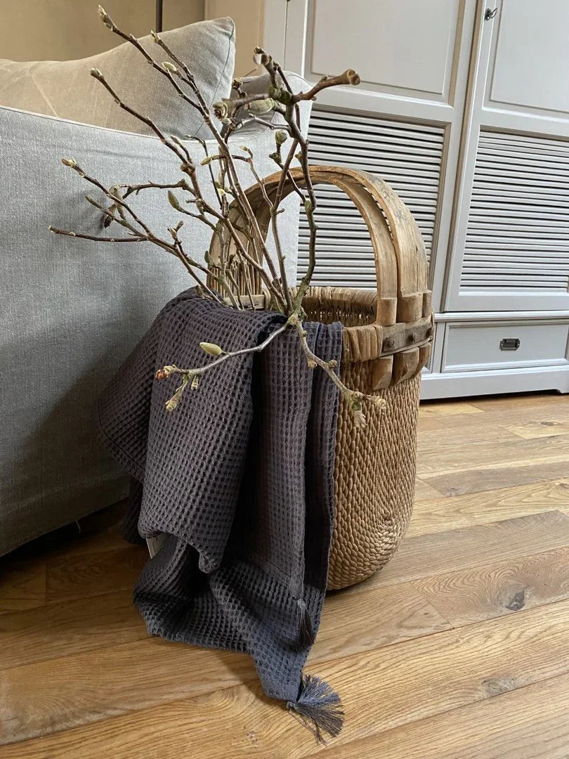 Handgemaakte plukmand met takken en donker plaid in landelijk sober interieur
