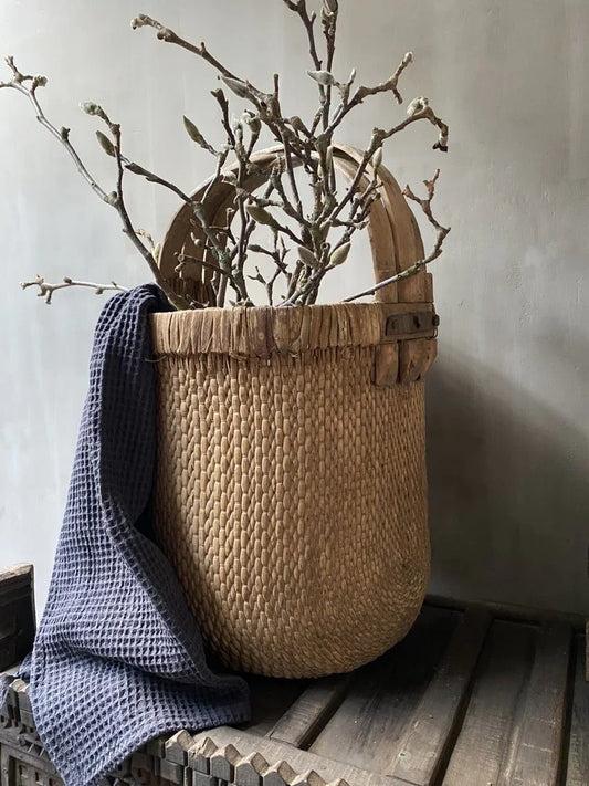 Handgemaakte rotan plukmand met takken en donkergrijze doek, landelijke woondecoratie