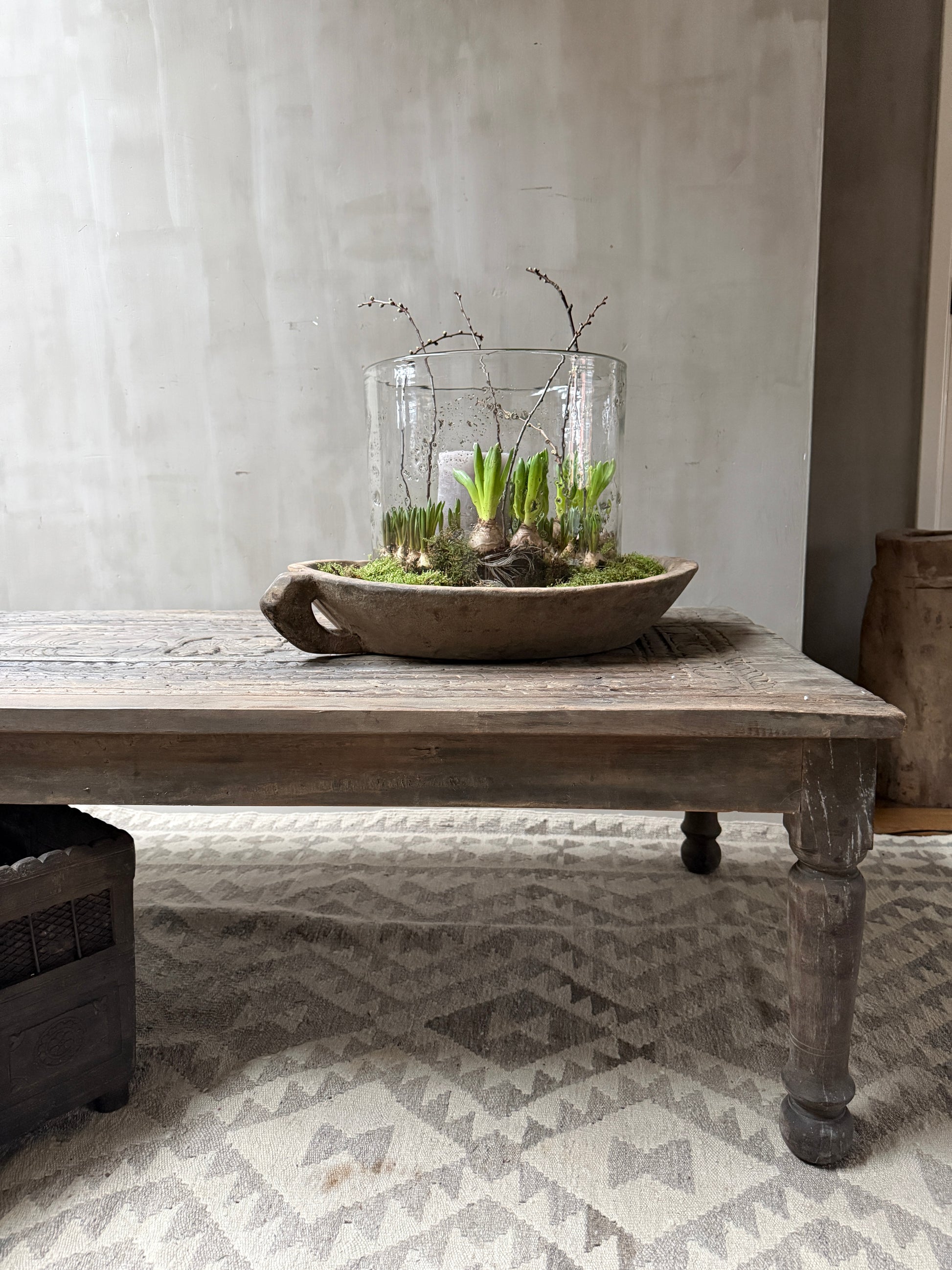 Handgemaakte houten salontafel met glazen vaas en groene planten, sober landelijk interieur