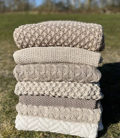 Stapel handgemaakte plaids in beige tinten op gras, landelijke woondecoratie My Sober Home