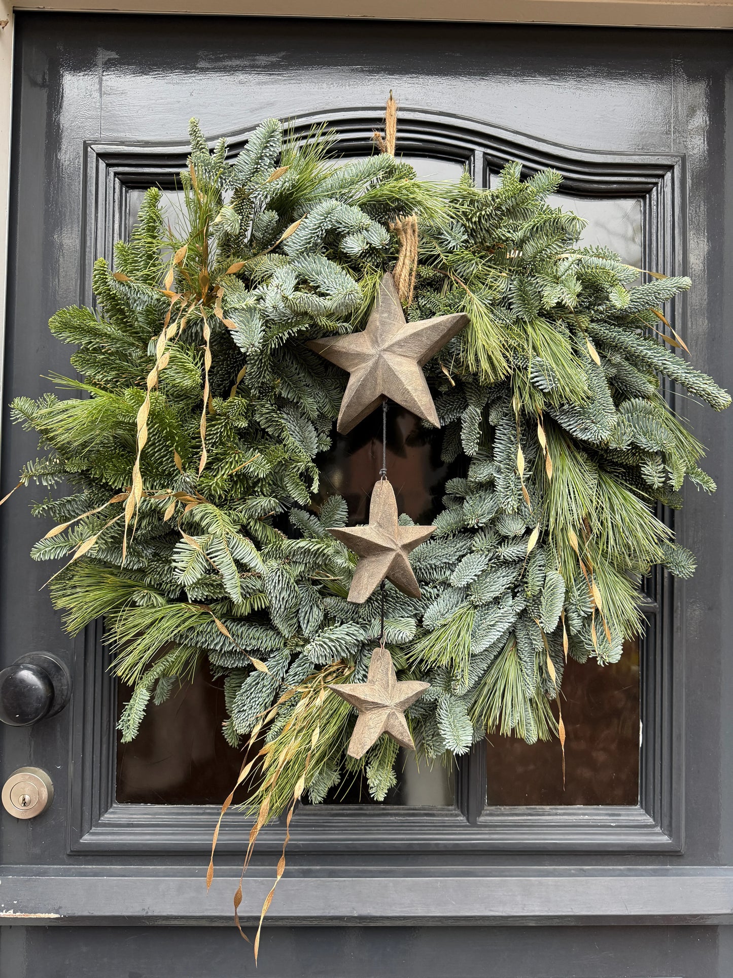 Handgemaakte groene krans met houten sterhanger op donkere deur, landelijk woonaccessoire.