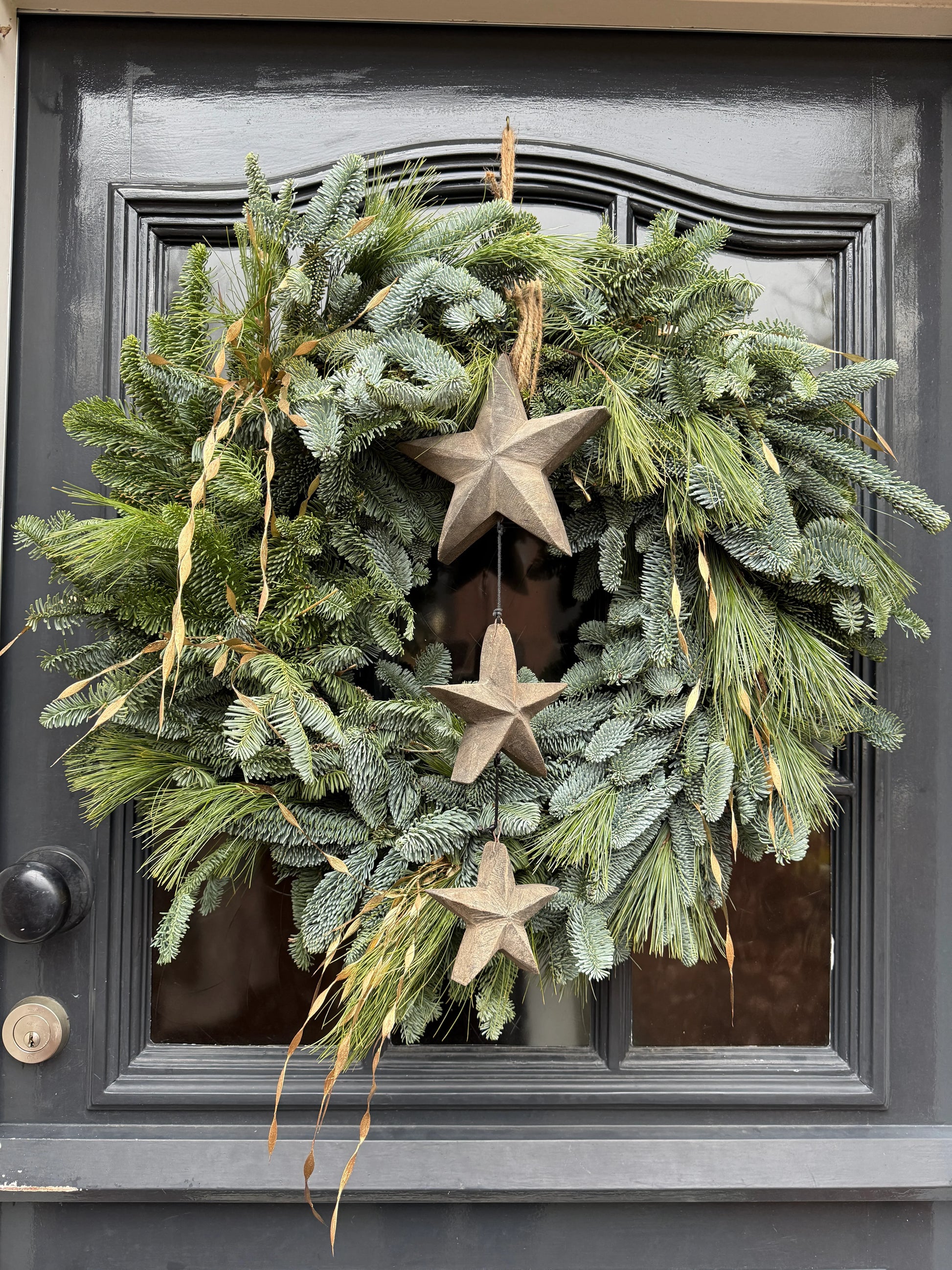 Handgemaakte groene krans met houten sterhanger op donkere deur, landelijk woonaccessoire.