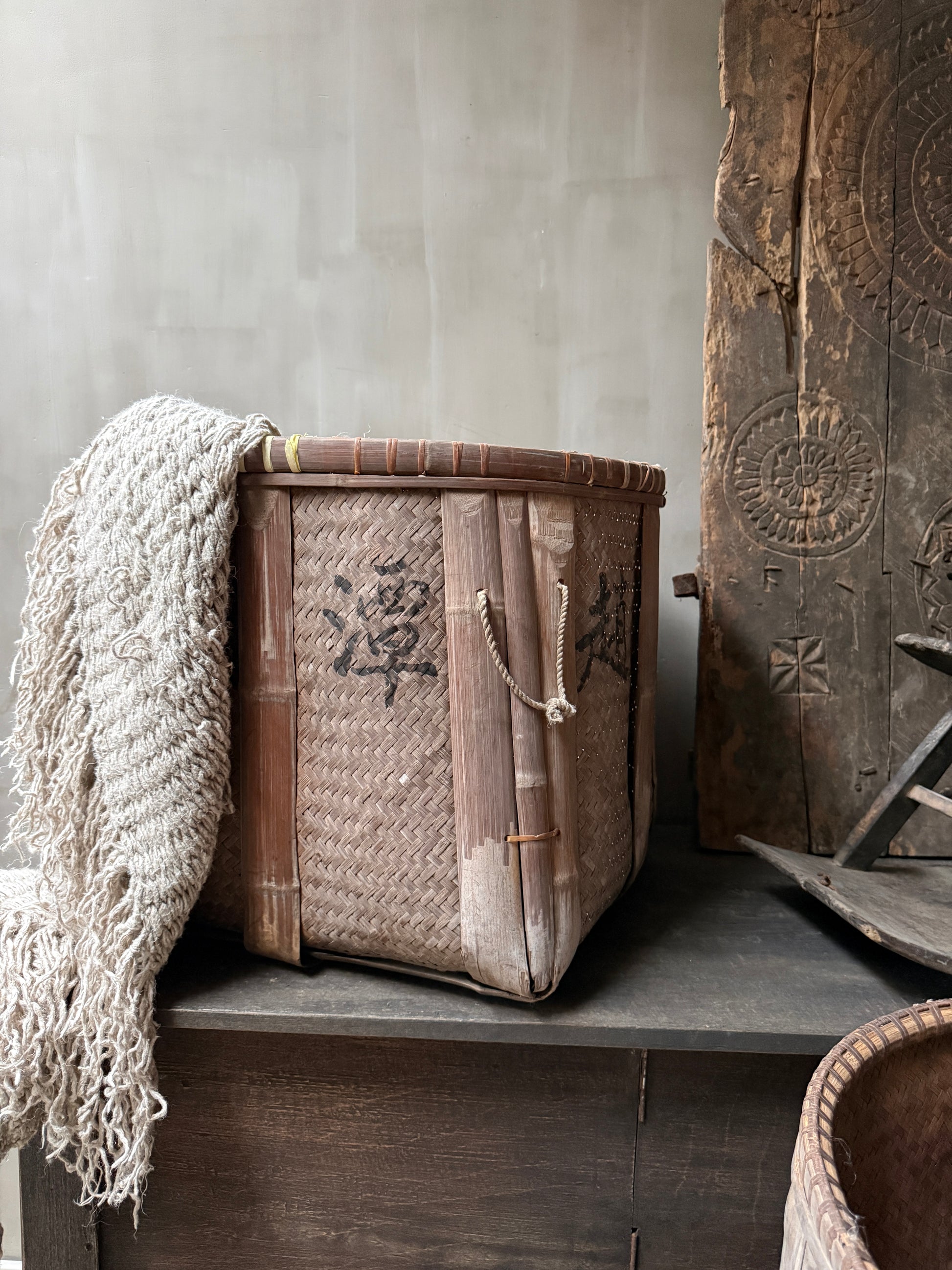 Handgemaande vintage mand van bamboe met landelijke uitstraling, beige plaid eroverheen.