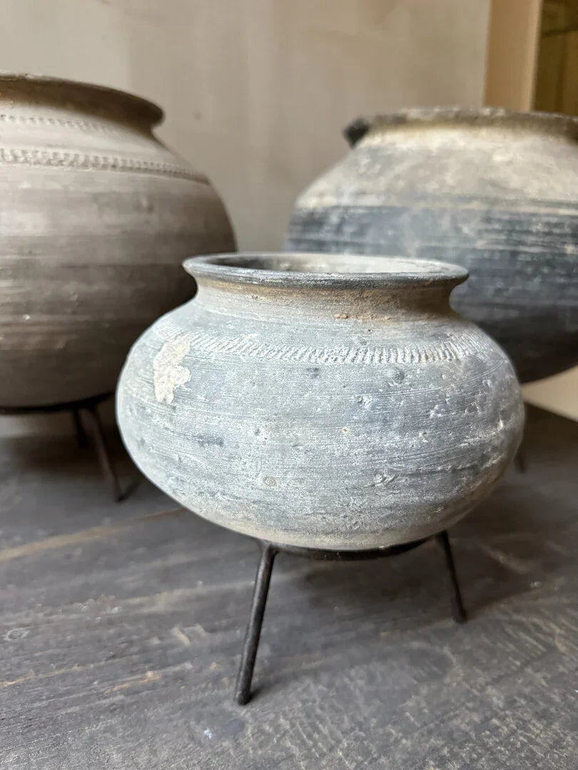 Oude, handgemaakte tuimelkruik van aardewerk op metalen standaard, landelijke woondecoratie.