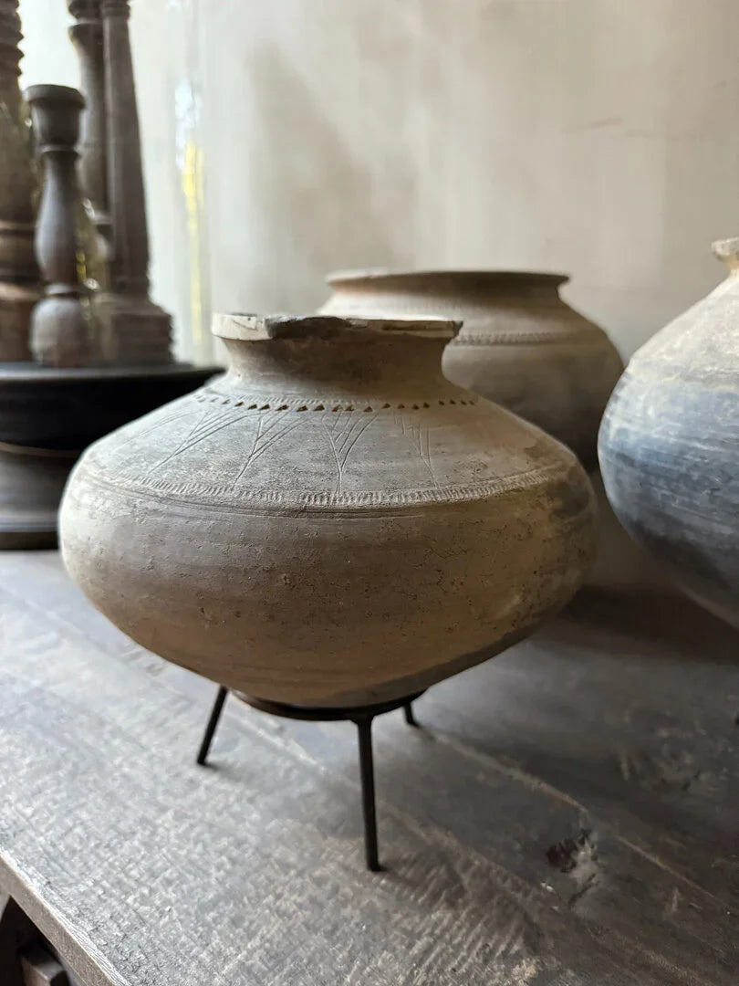 Authentieke handgemaakte tuimelkruik van aardewerk op metalen standaard, sober landelijk interieur