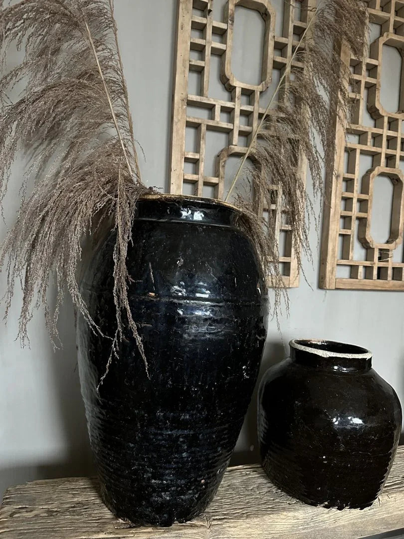 Zwarte handgemaakte vazen met siergras op houten plank, landelijk en sober interieurdecoratie.