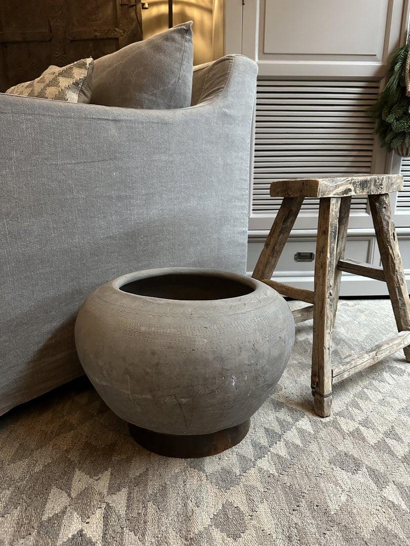 Handgemaakte sobere Wankelpot ring vaas op tapijt bij landelijke houten kruk en grijze bank.