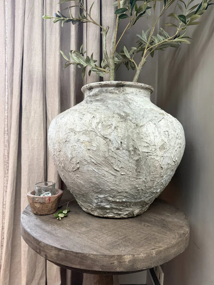 Handgemaakte landelijke waterkruik met takken op houten tafel, sober interieuraccessoire.