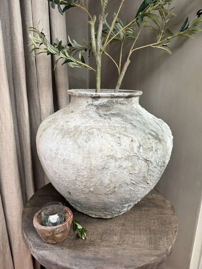 Authentieke, handgemaakte waterkruik met takken op houten tafel, landelijk sober interieur.