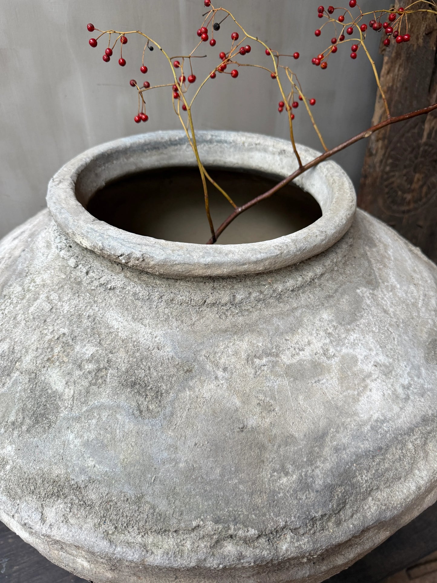 Authentieke handgemaakte grijze waterpot met rode bessen, sober landelijk interieur