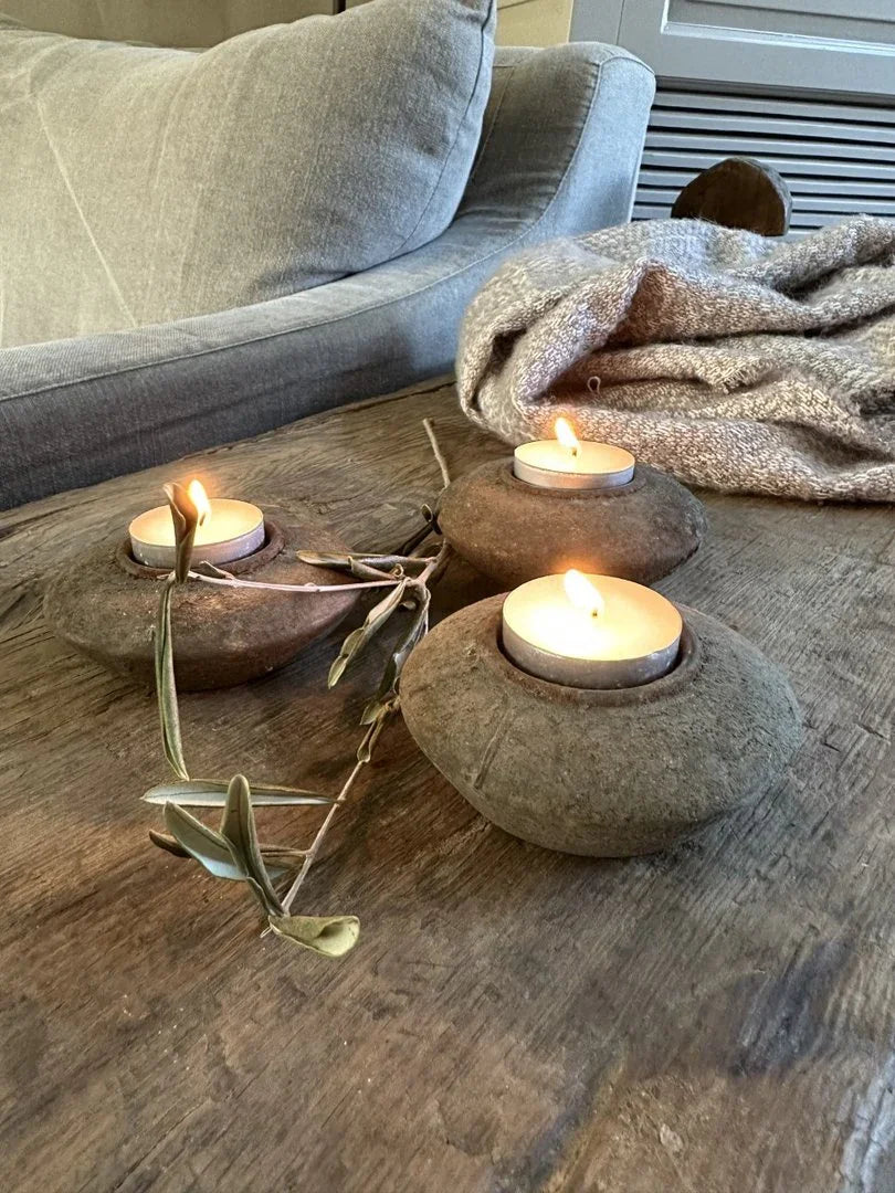 Handgemaakte stenen waxinelichthouders met brandende kaarsjes op houten tafel, landelijk sober interieur