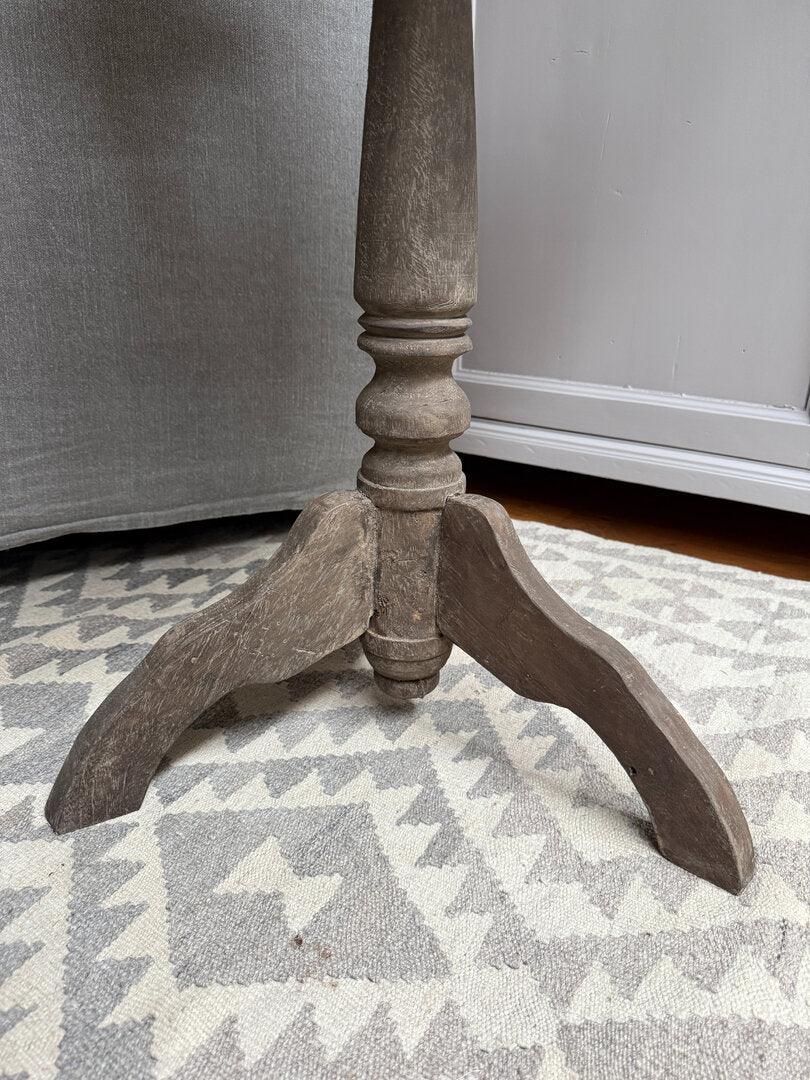 Houten wijntafelpoot met verweerde look op lichtgrijs vloerkleed, sober landelijk interieur