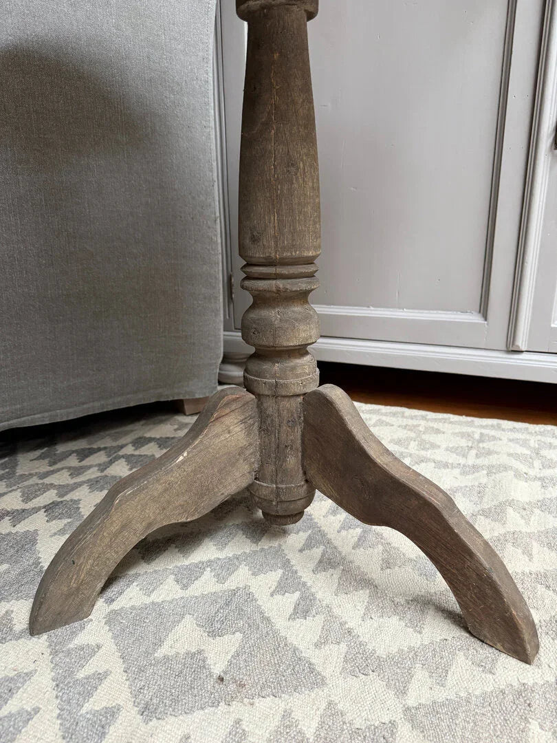 Authentieke houten wijntafelpoot op licht oosters vloerkleed, sober landelijk interieur