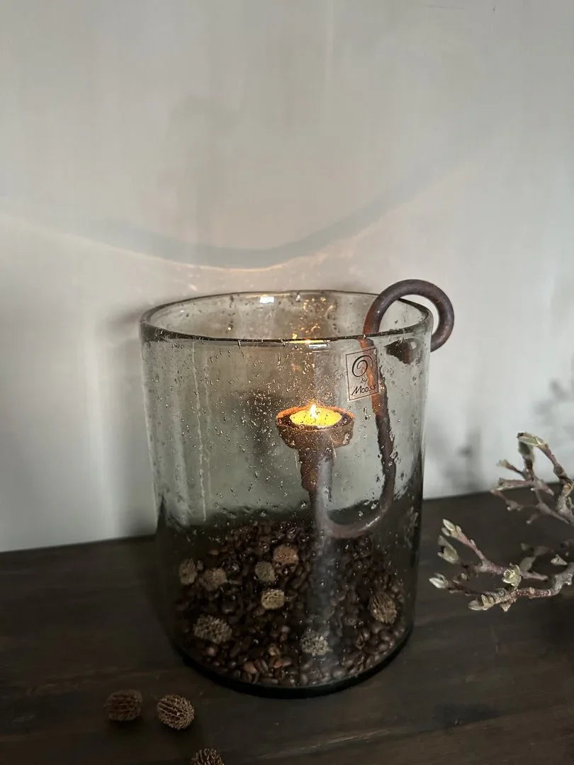 Windlicht van glas met brandend kaarsje en landelijke vulling, sfeervol sober woonaccessoire