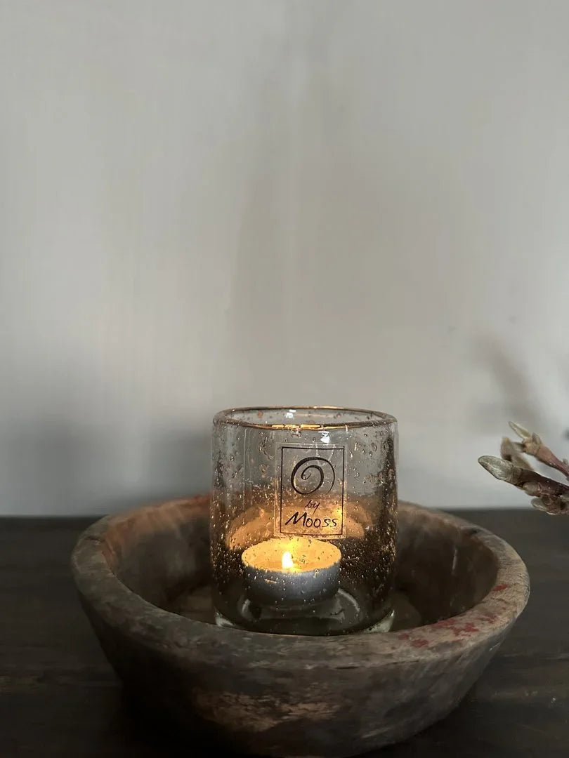 Handgemaakt windlicht van glas met brandend waxinelichtje in houten schaal, sober interieur