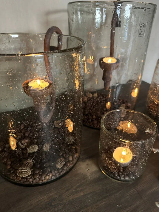 Handgemaakte glazen windlichten met steenslag en brandende kaarsen op houten tafel, landelijk sober interieur