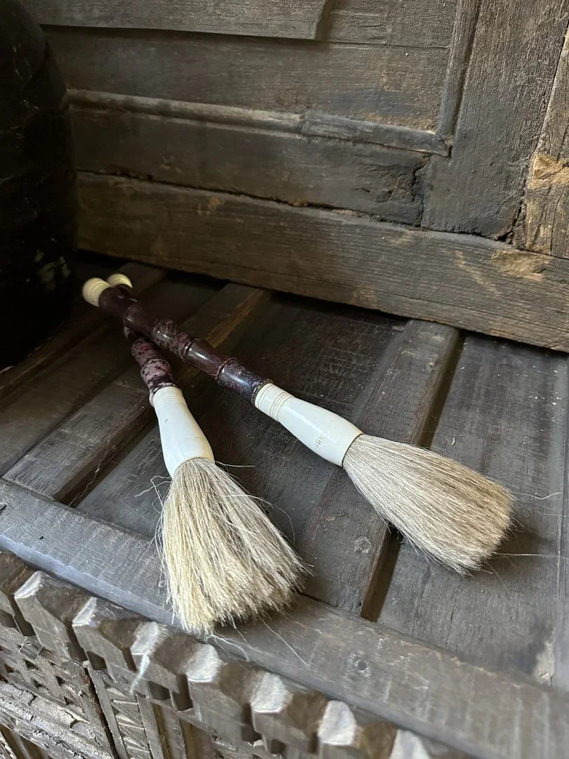 Twee authentieke kalligrafeerkwasten met houten handvat op een rustieke houten kast, sober interieur