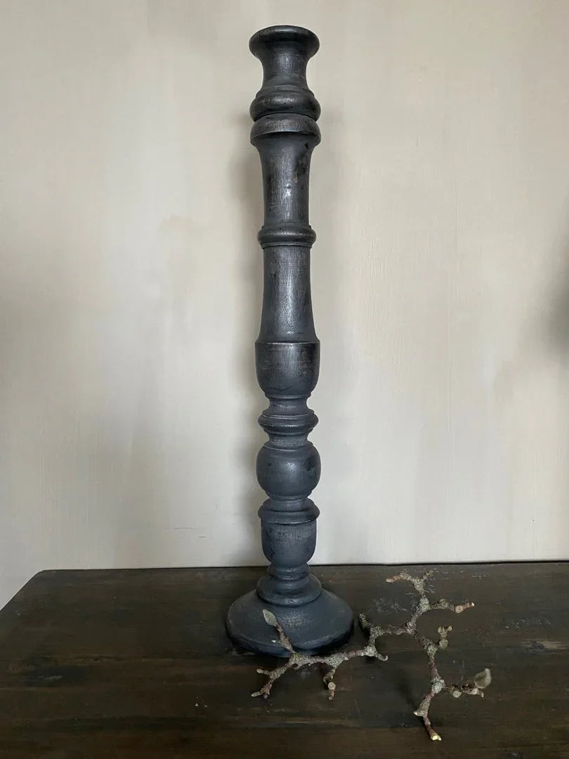 Zwarte houten kandelaar, handgemaakt, op donker houten tafel in sober landelijk interieur